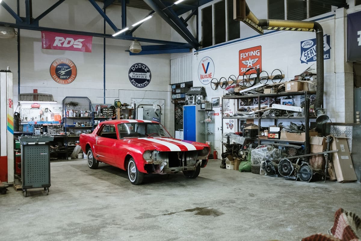 Classic car in a workshop surrounded by shelves of parts